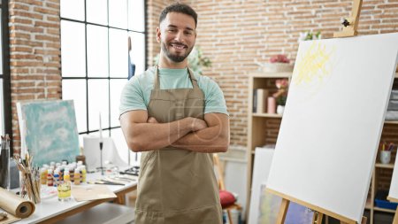 Photo for Young arab man artist standing with arms crossed gesture smiling at art studio - Royalty Free Image
