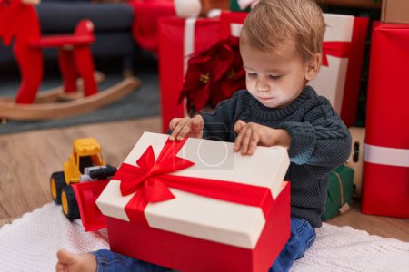 Photo for Adorable blond toddler unpacking christmas gift sitting on floor at home - Royalty Free Image