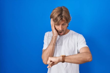 Photo for Middle age man standing over blue background looking at the watch time worried, afraid of getting late - Royalty Free Image