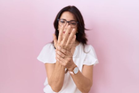Photo for Middle age hispanic woman wearing casual white t shirt and glasses suffering pain on hands and fingers, arthritis inflammation - Royalty Free Image