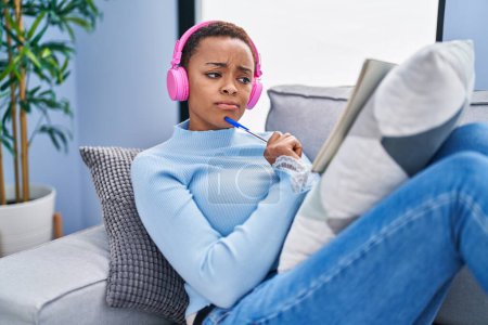 Foto de African american woman listening to music writing on notebook at home - Imagen libre de derechos