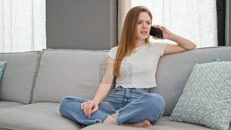 Téléchargez les photos : Jeune femme blonde parlant sur un smartphone assis sur un canapé se disputant à la maison - en image libre de droit