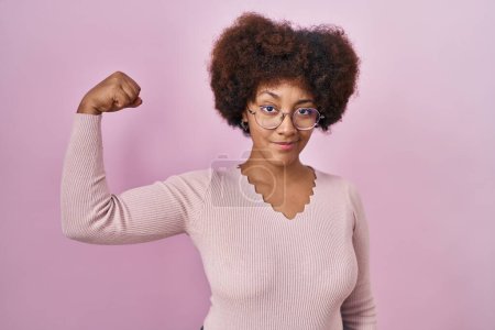 Téléchargez les photos : Jeune femme afro-américaine debout sur fond rose personne forte montrant muscle du bras, confiant et fier de la puissance - en image libre de droit