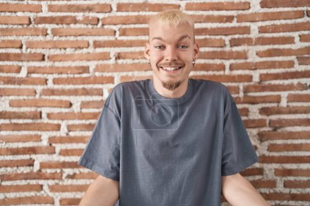 Photo for Young caucasian man standing over bricks wall smiling cheerful with open arms as friendly welcome, positive and confident greetings - Royalty Free Image