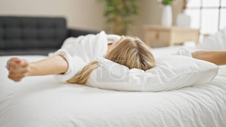 Foto de Joven mujer rubia despertando estirando los brazos en el dormitorio - Imagen libre de derechos