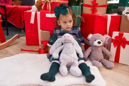 Foto de Adorable niño rubio sentado en el suelo por regalos de Navidad con expresión relajada en casa - Imagen libre de derechos