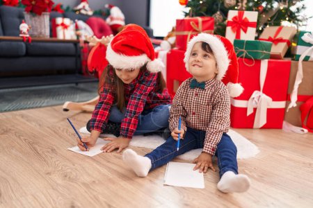 Photo for Adorable boy and girl drawing on paper celebrating christmas at home - Royalty Free Image