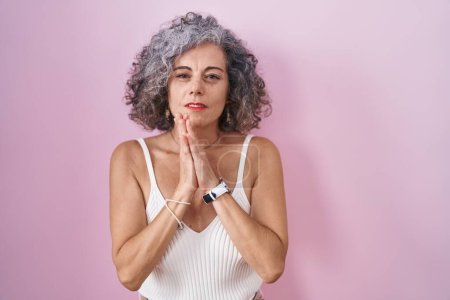 Téléchargez les photos : Middle age woman with grey hair standing over pink background begging and praying with hands together with hope expression on face very emotional and worried. begging. - en image libre de droit