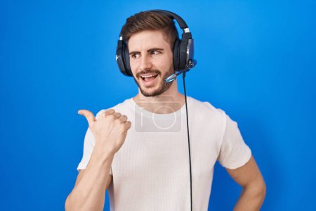 Photo for Hispanic man with beard listening to music wearing headphones smiling with happy face looking and pointing to the side with thumb up. - Royalty Free Image