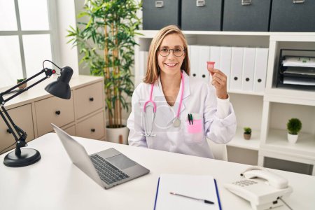 Photo for Young blonde doctor woman holding menstrual cup looking positive and happy standing and smiling with a confident smile showing teeth - Royalty Free Image