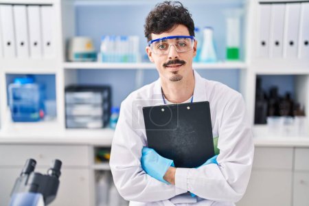 Photo for Young caucasian man scientist smiling confident holding clipboard at laboratory - Royalty Free Image