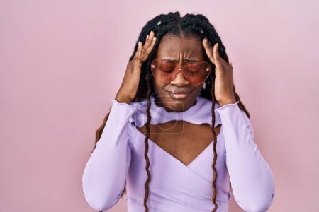 Foto de Mujer africana con el pelo trenzado de pie sobre fondo rosa con la mano en la cabeza para el dolor en la cabeza porque el estrés. padecer migraña. - Imagen libre de derechos