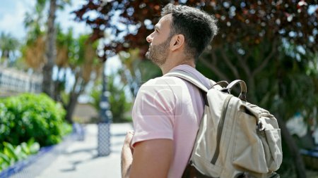 Téléchargez les photos : Jeune homme hispanique touriste portant un sac à dos regardant autour en souriant au parc - en image libre de droit
