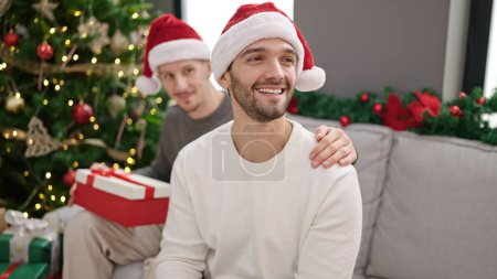 Téléchargez les photos : Deux hommes couple célébrant Noël tenant cadeau à la maison - en image libre de droit