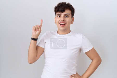 Téléchargez les photos : Jeune homme non binaire portant T-shirt blanc décontracté pointant du doigt avec une idée réussie. Sorti et heureux. numéro un. - en image libre de droit