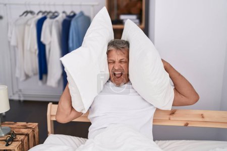 Photo for Middle age grey-haired man covering ears for noise at bedroom - Royalty Free Image