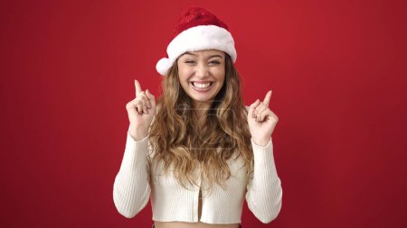 Photo for Young beautiful hispanic woman wearing christmas hat pointing with fingers raised up over isolated red background - Royalty Free Image