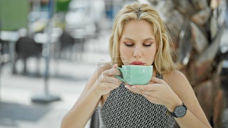 Téléchargez les photos : Jeune femme blonde buvant une tasse de café assise sur la table de la terrasse du café - en image libre de droit