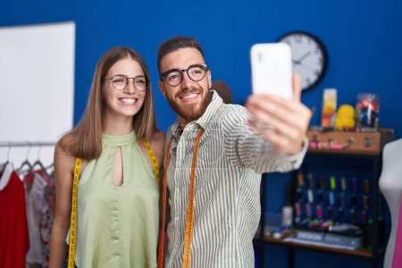Foto de El hombre y la mujer sastres sonriendo confiado hacer selfie por teléfono inteligente en la fábrica de ropa - Imagen libre de derechos