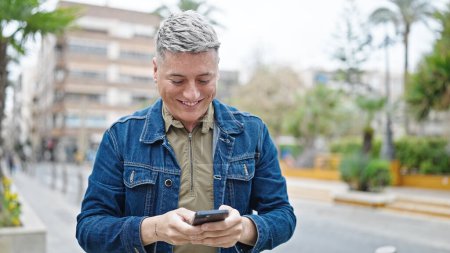 Foto de Joven hombre caucásico usando teléfono inteligente sonriendo en la calle - Imagen libre de derechos