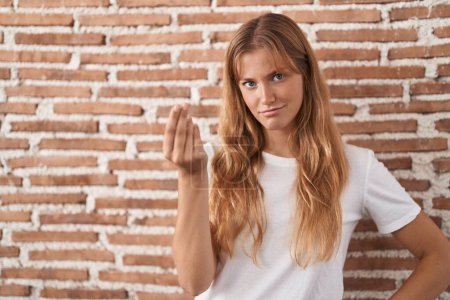 Téléchargez les photos : Jeune femme caucasienne debout sur le mur de briques faisant geste italien avec la main et les doigts expression confiante - en image libre de droit