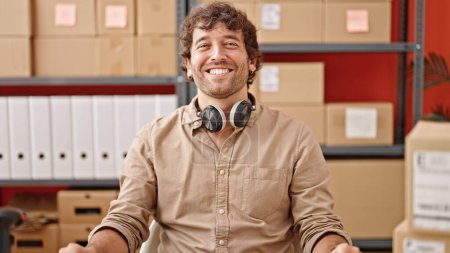 Téléchargez les photos : Jeune homme hispanique commerce électronique travailleur d'affaires assis sur la table souriant au bureau - en image libre de droit