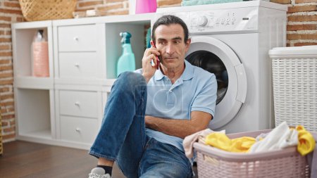Téléchargez les photos : Moyen Age homme parlant sur smartphone en attente de machine à laver à la buanderie - en image libre de droit