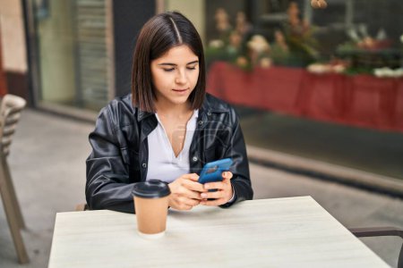 Foto de Mujer hispana hermosa joven usando teléfono inteligente sentado en la mesa en la terraza de la cafetería - Imagen libre de derechos