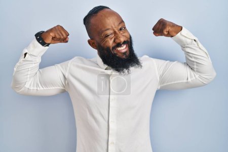 Téléchargez les photos : Homme afro-américain debout sur fond bleu montrant les muscles des bras souriant fier. concept de fitness. - en image libre de droit