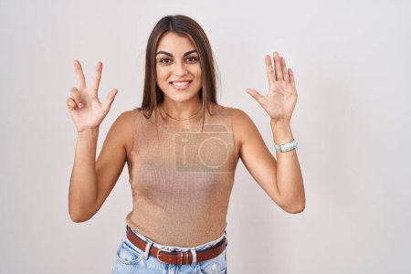 Photo for Young hispanic woman standing over white background showing and pointing up with fingers number eight while smiling confident and happy. - Royalty Free Image