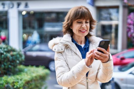 Foto de Mujer de mediana edad sonriendo confiado usando teléfono inteligente en la calle - Imagen libre de derechos
