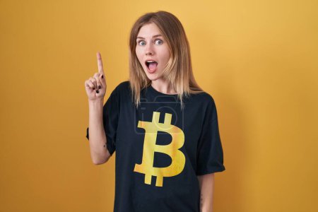 Téléchargez les photos : Blonde femme caucasienne portant Bitcoin t-shirt pointant du doigt avec une idée réussie. Sorti et heureux. numéro un. - en image libre de droit