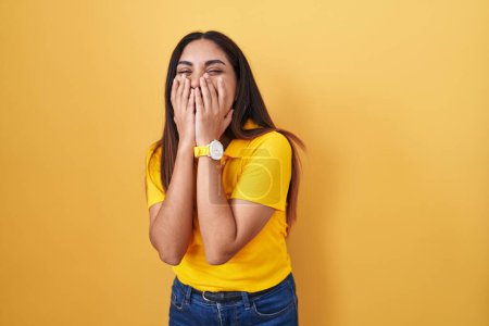 Téléchargez les photos : Jeune femme arabe debout sur fond jaune rire et rire embarrassé couvrant la bouche avec les mains, commérages et concept scandale - en image libre de droit