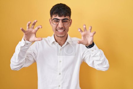 Téléchargez les photos : Young hispanic man standing over yellow background smiling funny doing claw gesture as cat, aggressive and sexy expression - en image libre de droit