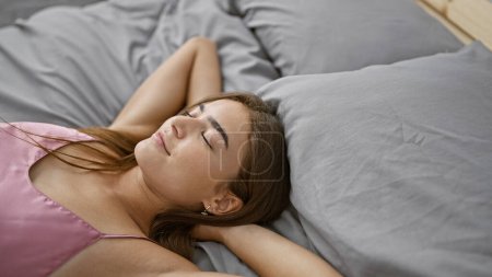 Téléchargez les photos : Jeune femme hispanique détendue confortablement allongée au lit, les mains reposant sur sa tête, profitant d'une matinée confortable dans sa chambre - en image libre de droit
