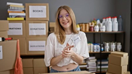 Téléchargez les photos : Jeune femme blonde bénévole souriant confiant applaudissements mains au centre de charité - en image libre de droit