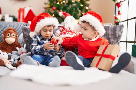Photo for Two kids holding gift sitting on sofa by christmas tree at home - Royalty Free Image