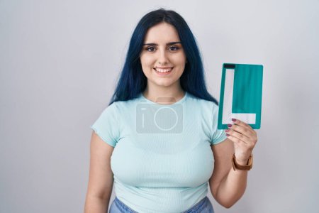 Photo for Young modern girl with blue hair holding l sign for new driver looking positive and happy standing and smiling with a confident smile showing teeth - Royalty Free Image