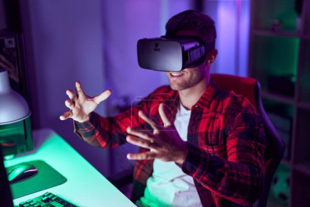 Téléchargez les photos : Jeune homme caucasien streamer jouer à un jeu vidéo en utilisant des lunettes de réalité virtuelle à la salle de jeu - en image libre de droit