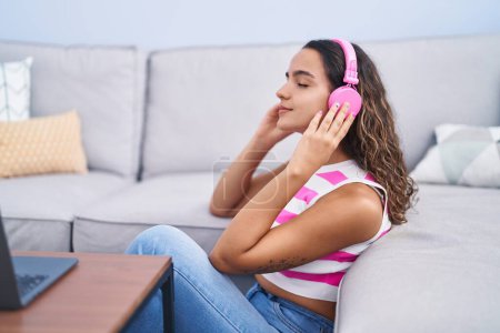 Photo for Young beautiful hispanic woman listening to music sitting on sofa at home - Royalty Free Image