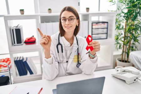 Photo for Young caucasian doctor woman holding support red ribbon smiling happy pointing with hand and finger to the side - Royalty Free Image