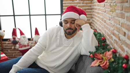 Foto de Hombre afroamericano durmiendo en sofá usando sombrero de navidad en casa - Imagen libre de derechos