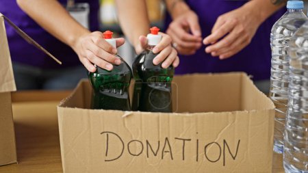 Téléchargez les photos : Mains de bénévoles mettant des produits sur la boîte en carton des dons au centre de bienfaisance - en image libre de droit