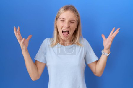 Photo for Young caucasian woman wearing casual blue t shirt celebrating mad and crazy for success with arms raised and closed eyes screaming excited. winner concept - Royalty Free Image