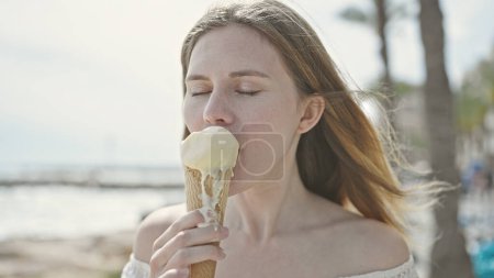 Foto de Joven mujer rubia turista comiendo helado en la playa - Imagen libre de derechos