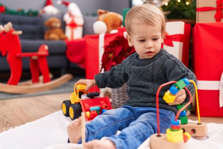 Foto de Adorable niño rubio jugando con juguetes sentados en el suelo por regalos de Navidad en casa - Imagen libre de derechos