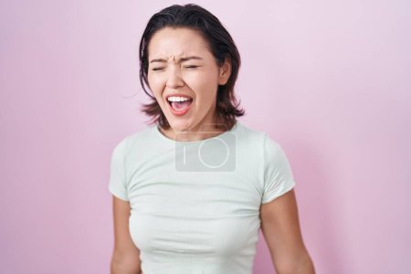 Photo for Hispanic young woman standing over pink background angry and mad screaming frustrated and furious, shouting with anger. rage and aggressive concept. - Royalty Free Image