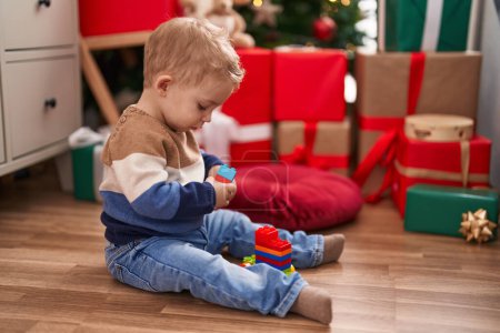 Foto de Adorable niño jugando con bloques de construcción sentado en el suelo por regalos de Navidad en casa - Imagen libre de derechos