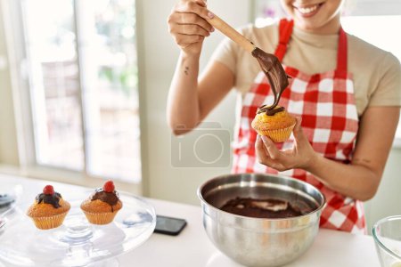 Photo for Young beautiful hispanic woman smiling confident putting chocolate on muffin at the kitchen - Royalty Free Image