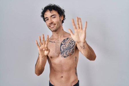 Foto de Hombre hispano de pie sin camisa mostrando y señalando hacia arriba con los dedos número nueve mientras sonríe confiado y feliz. - Imagen libre de derechos